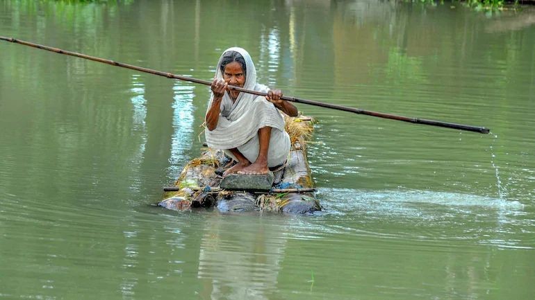 An elderly woman rows a makeshift raft to cross a flood-affected area of Mayoong village in Morigaon district of Assam. (PTI Photo)